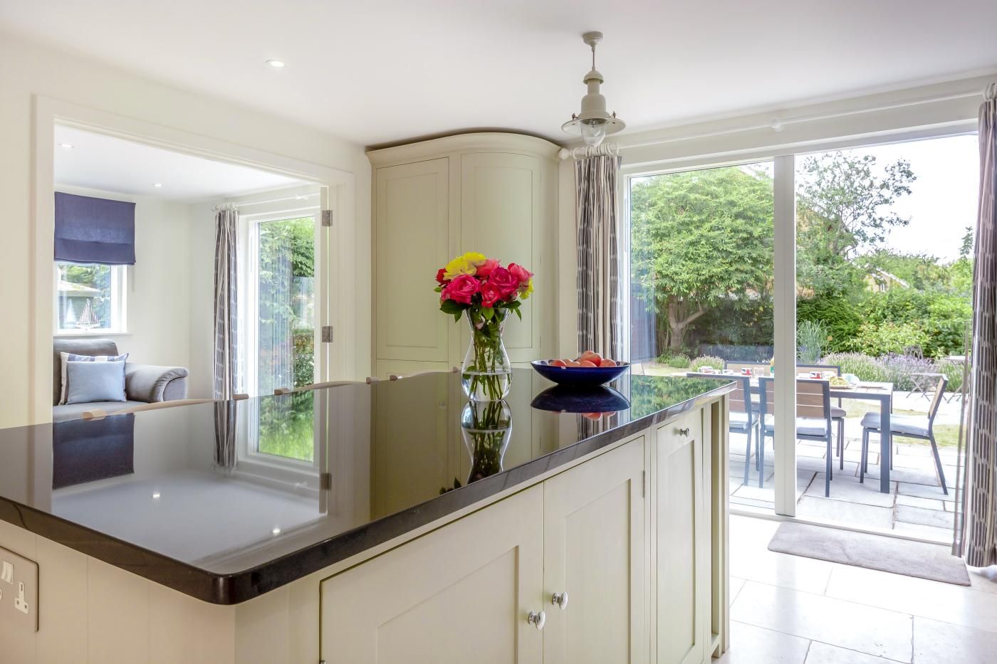 A modern kitchen with a large island, a dining area with outdoor seating, and a view of the garden.