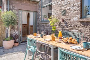 An outdoor dining area with a wooden table set for breakfast, surrounded by stone walls and potted plants. - 5 Bed in Bwlch (oc-p32273) (Bwlch)