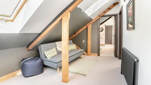 Ein Schlafzimmer im Loft-Stil mit Schräge, einem grauen Sofa, einer Holzbalkenkonstruktion und einer Heizung.
