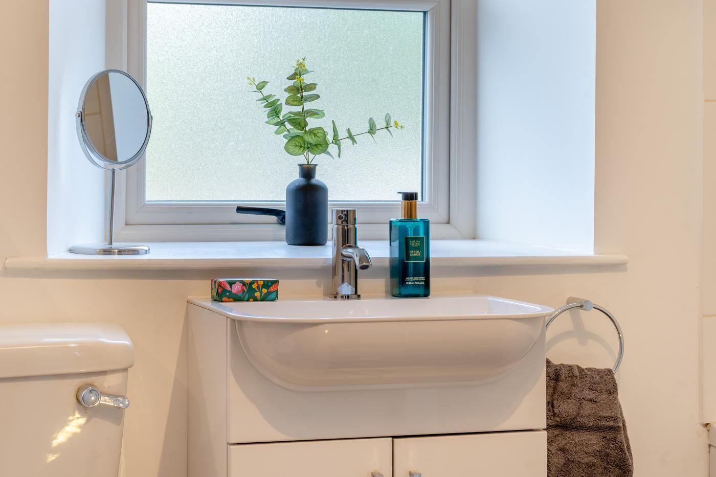 Ein Badezimmer mit Waschbecken, Spiegel, Topfpflanze und Handseife.