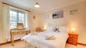 A bedroom with a bed, bedside tables, a dresser, a window with curtains, and wall art. - 2 Bed in Sheringham (oc-2029) (Sheringham)
