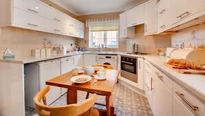 A modern kitchen with white cabinetry, a wooden dining table, and a built-in oven. - 2 Bed in Sheringham (oc-2029) (Sheringham)
