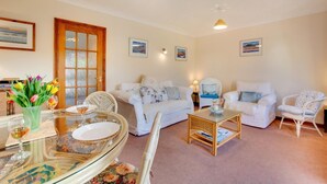 A cozy living room with a glass dining table, two white sofas, and a wicker coffee table. - 2 Bed in Sheringham (oc-2029) (Sheringham)