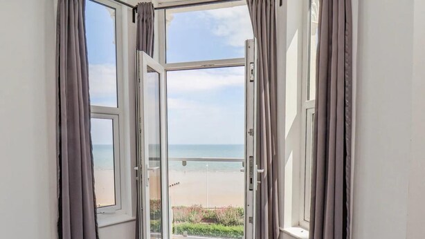 Een kamer met een grote glazen deur die uitkomt op een balkon met uitzicht op het strand.