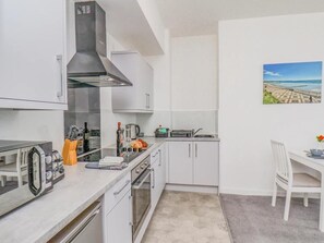 A compact kitchen with white cabinets, a gas stove, a microwave, and a small dining area with a chair and table. - 1 Bed in Bridlington (oc-o32013) (Bridlington)
