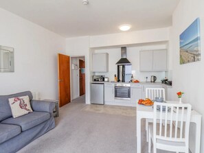 A compact living space with a kitchenette, a grey sofa, a white dining table, and a white chair. - 1 Bed in Bridlington (oc-o32013) (Bridlington)