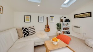 Ein modernes Wohnzimmer mit einem weißen Sofa, einem Couchtisch mit Obst, einer Gitarre und einem Bücherregal.