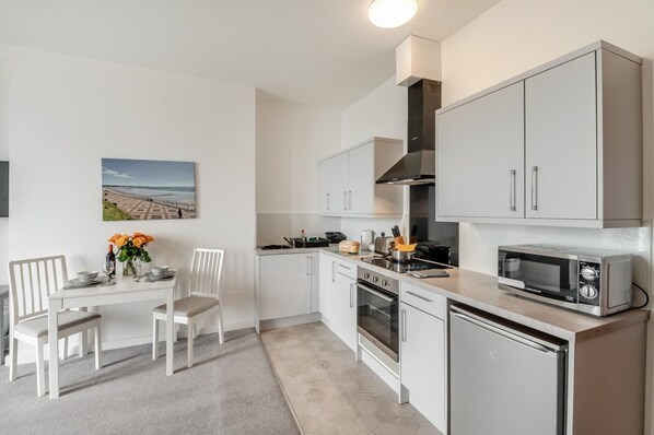 A modern kitchen with white cabinetry, a built-in oven, a microwave, and a dining area with a white table and chairs.