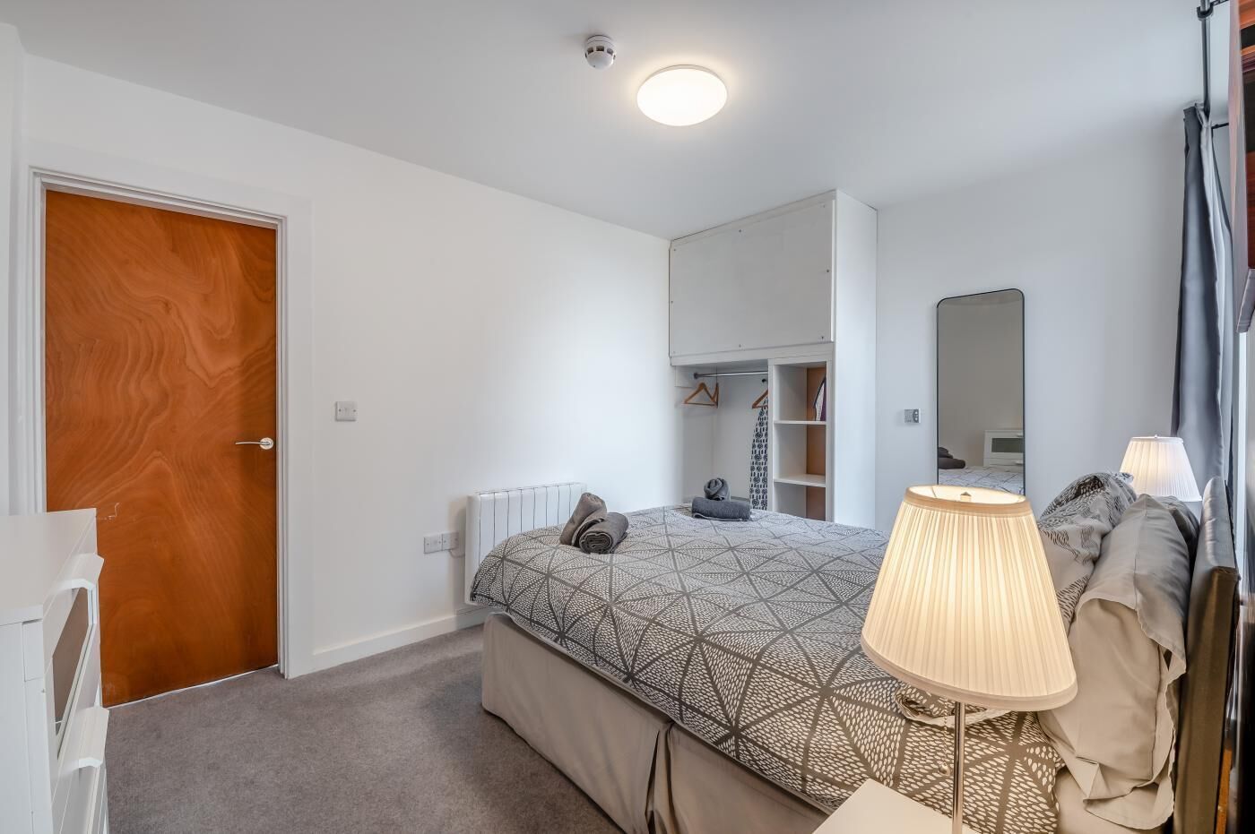 Une chambre à coucher comprenant un lit, une table de chevet, une lampe et une armoire.