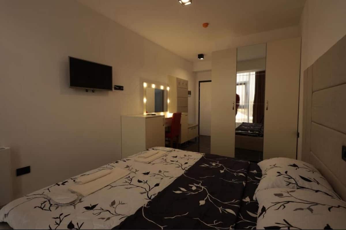 Una camera d'albergo con un letto, una televisione, uno specchio e una porta che dà su un'altra stanza.