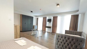 Una habitación amplia con una cama grande, un sofá tapizado de color gris, una mesa de comedor y una zona de cocina.