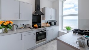 Eine moderne Küche mit weißen Schränken, einer schwarzen Dunstabzugshaube, einem großen Fenster mit Meerblick und einer Arbeitsplatte mit Toaster und Kaffeemaschine.