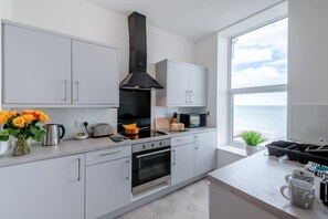 Eine moderne Küche mit weißen Schränken, einer schwarzen Dunstabzugshaube, einem großen Fenster mit Meerblick und einer Arbeitsplatte mit Toaster und Kaffeemaschine.