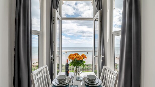 Ein Esstisch für zwei Personen mit Blick auf das Meer durch große Fenster.