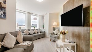Un salon moderne avec un canapé gris, un fauteuil à motifs et un téléviseur à écran plat fixé à un mur en bois.
