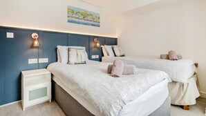 Une chambre d’hôtel moderne avec deux lits, une table de chevet et des lampes fixées au mur.