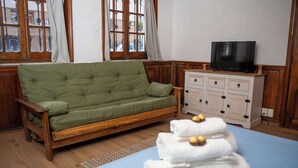 Una habitación con un sofá verde, un armario de madera, un televisor y una pila de toallas.