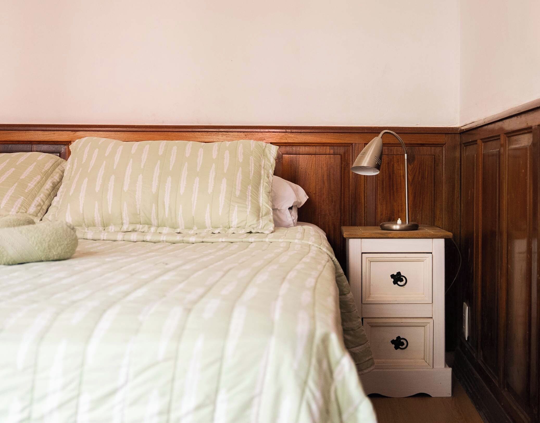 A bed with a striped bedspread and pillows, a bedside lamp, and a nightstand with drawers.