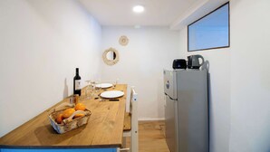 Una cocina funcional con una mesa de madera, un refrigerador, una tetera y una cesta de naranjas.