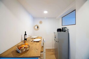 A compact kitchen with a wooden table, a refrigerator, a kettle, and a basket of oranges. - Casa Yacumenza Ground Floor CoastFlat (Montevideo)