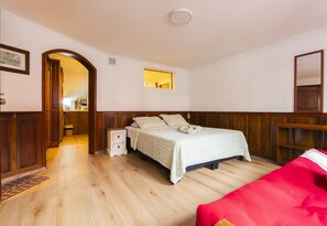 A bedroom with a wooden floor, a bed with a white bedspread, a red chair, and a wooden wardrobe. - Casa Yacumenza Ground Floor CoastFlat (Montevideo)