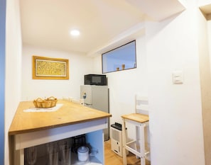 A compact kitchen with a wooden table, a microwave, a refrigerator, and a small window.