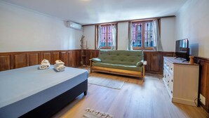 Una habitación con una cama, un sofá verde, un aparador de madera y un televisor.