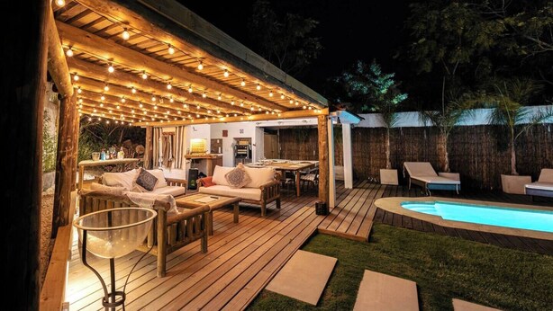 A wooden deck with outdoor furniture, a pool, and a covered seating area with string lights.