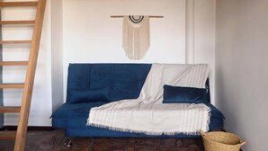 Ein blaues Sofa mit einer weiß-blauen Decke, eine Holzleiter und eine Wandbehagung aus Makramee.