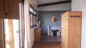 Eine schmale Küche mit Spüle, einem Fenster mit Vorhängen, einem Holzschrank und einer kleinen Essecke mit Tisch und Stühlen.