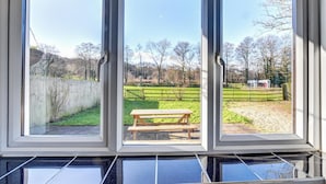 A view through a window with a wooden bench in the center, surrounded by a grassy area and a fence. - 2 Bed in Cardiff (oc-45378) (Gwern-y-Steeple)
