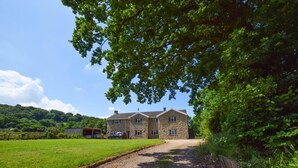 A stone house with a gravel driveway, surrounded by lush greenery and a clear sky. - 2 Bed in Cardiff (oc-45378) (Gwern-y-Steeple)
