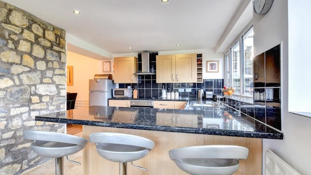 A modern kitchen with a stone accent wall, stainless steel appliances, and a black countertop. - 2 Bed in Cardiff (oc-45378) (Gwern-y-Steeple)