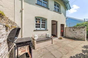 A two-story house with a patio area, a barbecue grill, a bench, and a door.