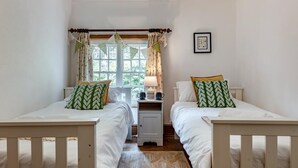 Ein Schlafzimmer mit zwei Einzelbetten, einem Schreibtisch und einem Fenster mit Vorhängen.
