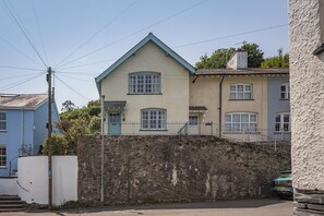 A two-story building with a steeply pitched roof, a stone wall in front, and a blue door.