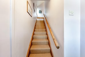 A staircase with carpeted steps and wooden handrails, leading to a landing with framed pictures and a sign.