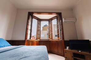 Une chambre à coucher avec un lit, une télévision et une fenêtre donnant sur des immeubles.