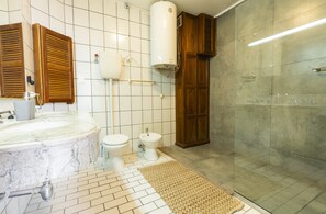 A bathroom with a marble sink, two toilets, a bidet, a shower, and wooden cabinets.