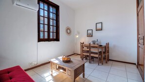 Ein kleiner, gut beleuchteter Raum mit einem Holztisch, einem roten Sofa und einem Fenster mit Jalousien.