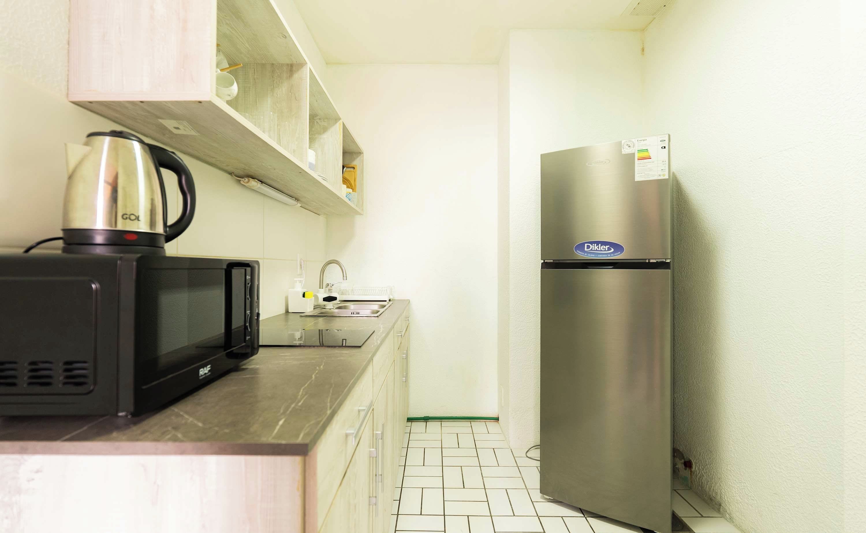 A compact kitchen with a microwave, kettle, and refrigerator.