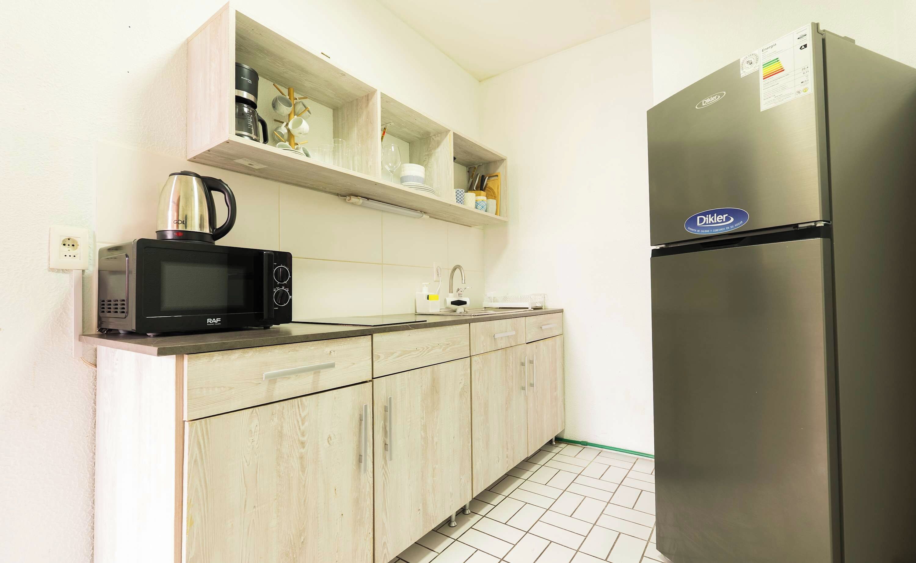 A kitchen with a microwave, kettle, and a refrigerator.