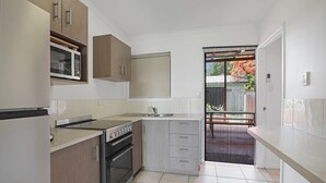 A compact kitchen with a stove, oven, and sink, wooden cabinets, and a sliding door leading to a balcony. - Unit tucked away in a quiet street (Amity)