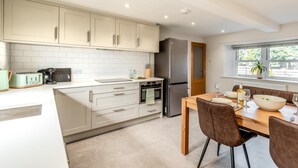 Una cocina moderna con armarios blancos, un refrigerador de acero inoxidable y un comedor con mesa y sillas de madera.