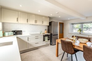 A modern kitchen with white cabinets, a stainless steel refrigerator, and a dining area with a wooden table and chairs. - 2 Bed in Dalston (oc-g32205) (Dalston)
