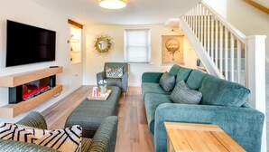 Una sala de estar con televisión, sofá, reposapiés y una escalera.