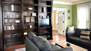 A living room with a dark wood bookshelf, a grey sofa, and a television. - Champlin House at Keuka Lake (Hammondsport)