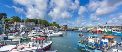 Un port où sont amarrés différents types de bateaux, avec des bâtiments en arrière-plan et un ciel dégagé.