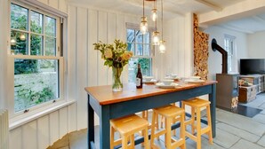 A kitchen with a wooden island, bar stools, a vase of flowers, and a wood-burning stove. - 2 Bed in Padstow (oc-p00821) (Padstow)