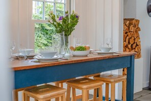 Ein Essbereich mit Holztisch, gedeckt für zwei Personen, einer Blumenvase und Blick ins Freie.